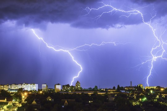 Lightning over the city in the night sky strikes the roof of the house