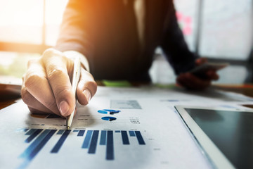 Close up Businessman hand holding pen and pointing at financial paperwork.