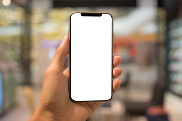 Close up of a man holding smartphone with blank screen mobile and laptop computer at coffee shop.