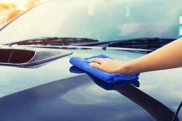 Asian woman's hand wiping surface of car by micro fiber cloth.