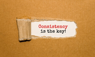 The text Consistency is the key appearing behind torn brown paper