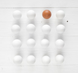 White raw eggs with one brown egg in rows on a white wooden table