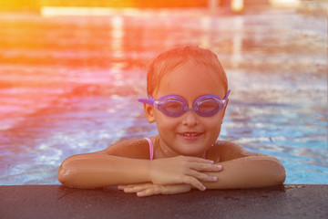 A happy young girl relaxing on the side of a swimming pool wearing goggles. Toned