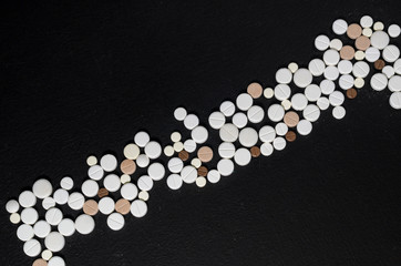 Handful of pills on a black background closeup, top view