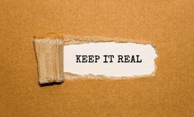 The text Keep It Real appearing behind torn brown paper