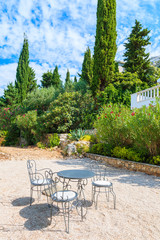Naklejka premium Three metal chairs with table on gravel patio in mediterranean garden near Primosten town, Dalmatia, Croatia