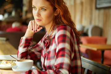 Smiling red hair woman reading book at coffee shop