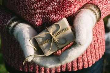 girl hands in white woollen mittens holding a gift box