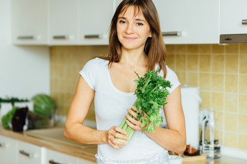 Healthy eating, cooking, vegetarian food, dieting and people concept - close up of young woman with celery in white kitchen interior.