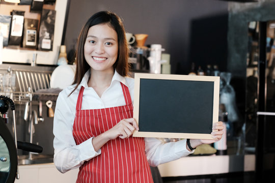 Young asian women Barista holding blank chalkboard menu with smiling face at cafe counter background, small business owner, food and drink industry concept