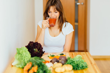 Healthy brunette woman drinking fresh detox Jjuice, Smoothie for breakfast. Closeup of beautiful smiling girl with vegetables at kitchen table. Nutrition concept.