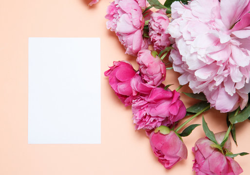 A bouquet of pink peonies and a sheet of white paper rests on a background of salmon-colored .
