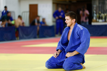 Judoka in blue judogi recovering after exhausting match