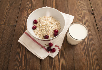 Bowl, bran, milk and fresh cherries, on wooden background, top view