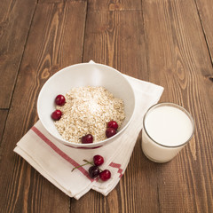 Bowl, bran, milk and fresh cherries, on wooden background, top view