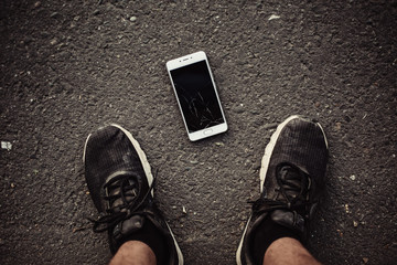 Legs and a smartphone with a broken screen on a dark background. The view from the top.