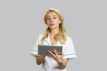 Portrait of serious nurse with pc tablet. Beautiful young female doctor with digital tablet on grey background.