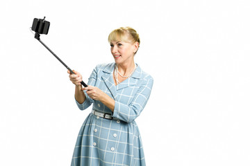 Mature woman using selfie stick. Beautiful smiling white-skin lady taking selfie isolated on white background.