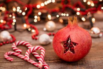 Christmas concept. Star pomegranate with candy in front of lights on wooden table.