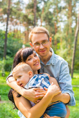 Fototapeta premium Dad hugs mom who holds the child in her arms. Happy family - Mom, Dad and child- for a walk in the park.