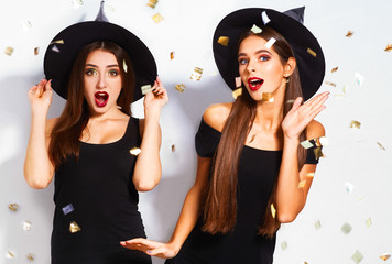 portrait of two happy young women in black witch halloween costumes on party over white background....
