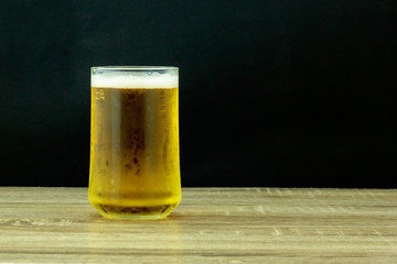 Glass beer on wooden table with black background