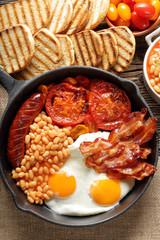English Breakfast with sausages, grilled tomatoes, egg, bacon and beans on frying pan.