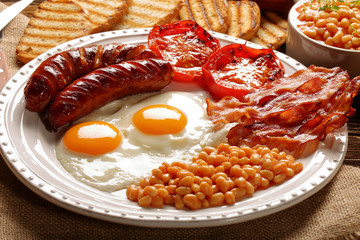 English Breakfast with sausages, grilled tomatoes, egg, bacon, beans and bread on white plate