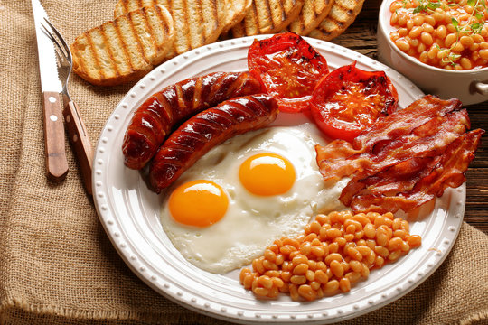 English Breakfast with sausages, grilled tomatoes, egg, bacon, beans and bread on white plate
