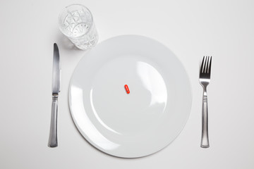 Red pill on a with plate with knife, fork and a glass of water isolated on white background
