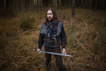 Knight in the forest. A guy in medieval costume with a sword