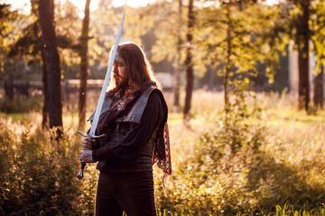 Knight in the forest. A guy in medieval costume with a sword