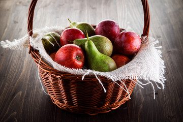 Fruit - apples, pears and plums in wicker basket on wooden table