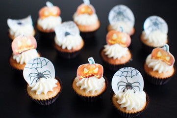 Halloween cupcakes and wooden table. Halloween cupcakes with decorations: tombstone, witch hat and pumpkins