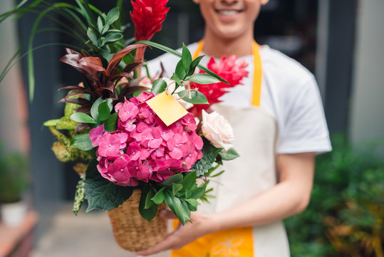 Handsome male florist is standing in flower shop and holding bouquet of flowers