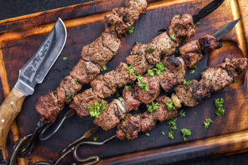 Traditional Russian shashlik on a barbecue skewer as top view on an old burnt cutting board