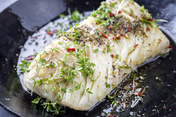 Fried cod fish fillet with spice and cress as close-up in a cast iron pan