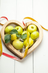 The concept of diet and healthy eating. A green apple and a centimeter on a white wooden background in the heart.