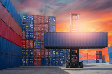 Forklift truck lifting cargo container in shipping yard or dock yard against sunrise sky with cargo...