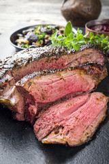 Barbecue haunch of venison with mushrooms and cranberry sauce as close-up on a slate slab