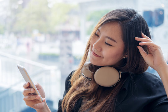 Closeup image portrait of a beautiful Asian woman using headphone and holding smart phone with feeling happy and relax in modern cafe