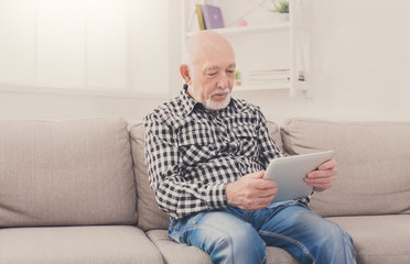 Senior man reading news on digital tablet