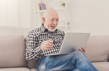 Naklejka premium Smiling senior man reading news on laptop