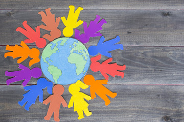 Friendship and peace concept, paper human figures and globe map on the wooden background.