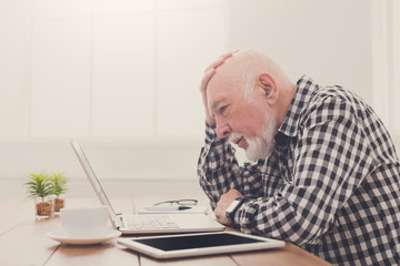 Worried senior man using laptop at home