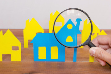 Buying or renting new house concept, colorful paper houses and magnifying glass in woman`s hand on...