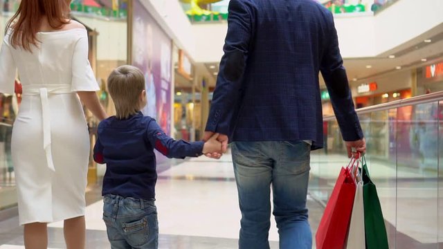 The boy holds a hand from the mother and the father. Parents not Sousse packages with Christmas gifts. Family Christmas shopping. The boy with parents go along the corridor shopping center. Christmas