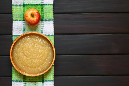 Homemade apple sauce in wooden bowl, photographed overhead on dark wood with natural light