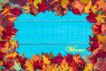 Welcome sign hanging on antique rustic teal blue wood background with colorful autumn leaves border; seasonal background with copy space