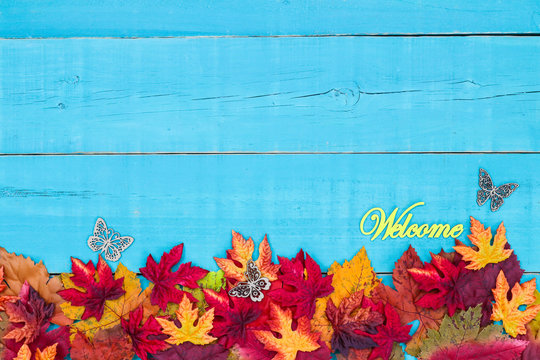 Welcome sign with butterfly on rustic teal blue wood background with colorful autumn leaves border